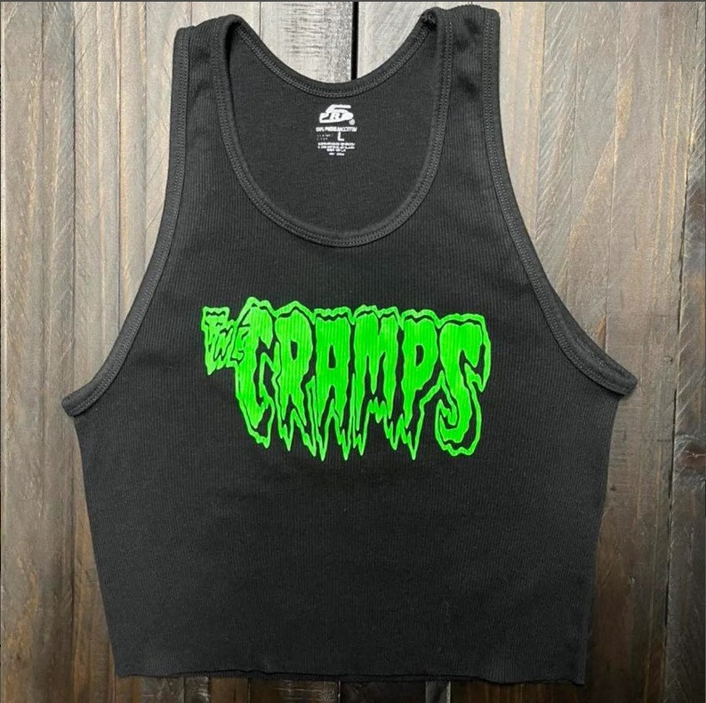 Pu&ograve; includere: Canotta nera a coste con la scritta verde neon "THE CRAMPS" sul davanti. La canotta ha uno scollo tondo ed &egrave; senza maniche. L'immagine &egrave; di una canotta corta, probabilmente per un abbigliamento casual.