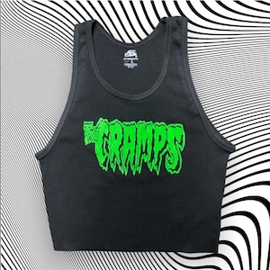 Pu&ograve; includere: Top corto nero a coste con la scritta verde neon "The Cramps" sul davanti. Il testo ha un font stilizzato a goccia. Il top ha uno scollo tondo e un design senza maniche. Lo sfondo &egrave; un motivo a strisce bianche e nere.