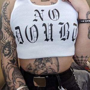 以下が含まれることがあります： 黒いゴシック体で「NO DOUBT」とプリントされた白いタンクトップ。タンクトップはクロップド丈で、リブの質感があります。