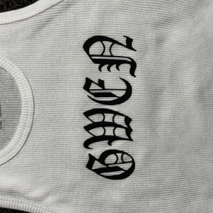 May include: White tank top with a black graphic of the word "SASS" in a stylized font.