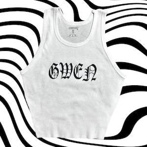 May include: White ribbed tank top with a black gothic font design that says "GWEN".