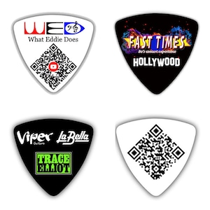 May include: Four different guitar picks with various designs. The first pick is white with a black and white QR code and the text "WE What Eddie Does". The second pick is black with a colorful design and the text "FAST TIMES 80's concert experience HOLLYWOOD". The third pick is black with the text "Viper Guitars La Bella" and a green rectangle with the text "TRACE ELLIOT". The fourth pick is white with a black and white QR code.