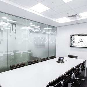 May include: A white conference room with a large screen displaying a graph. The room has a glass wall with a frosted design and a long white table with black chairs.