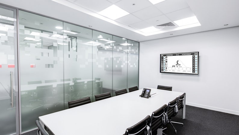 May include: A white conference room with a large screen displaying a graph. The room has a glass wall with a frosted design and a long white table with black chairs.