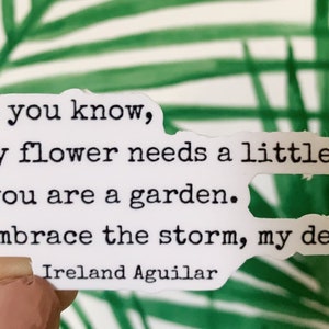 May include: A white sticker with black text that reads: "Don't you know, Every flower needs a little rain. And you are a garden. So, embrace the storm, my dear." The author's name, Ireland Aguilar, is at the bottom.