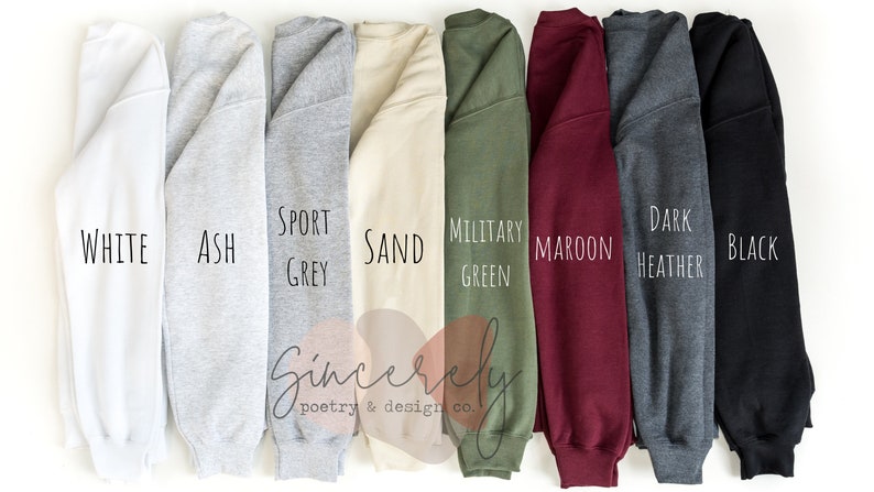 May include: A selection of eight different colored sweatshirts, including white, ash, sport grey, sand, military green, maroon, dark heather, and black. Each sweatshirt has the color name printed on it in a handwritten font. The brand name "Sincerely poetry & design co." is also visible.