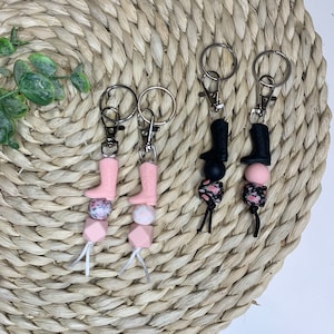 May include: Three pink and black boot-shaped keychains with floral and geometric beads. Each keychain has a silver ring and a silver clasp.
