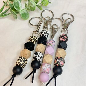May include: Three keychains with black, white, and brown beads. Each keychain has a different pattern: leopard print, black and white polka dots, and floral print. The keychains are attached to silver key rings.