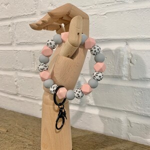 May include: A gray and pink silicone bracelet with a black paw print pattern. The bracelet has a black metal key chain attached.