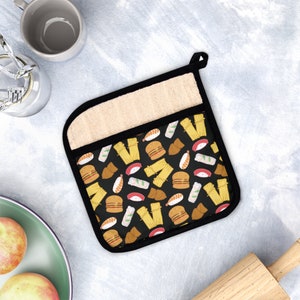 May include: A black and white pot holder with a pattern of sushi, spring rolls, and dumplings. The pot holder has a beige fabric backing.