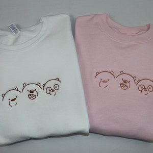 May include: Two sweatshirts with embroidered images of three cartoon bears. One sweatshirt is white and the other is pink.