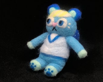 May include: A blue and white felt animal toy with a white shirt and blue pants. The toy has blue ears and a pink nose.