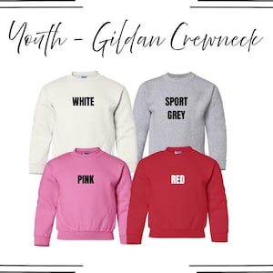May include: Four youth Gildan crewneck sweatshirts in white, sport grey, pink, and red. Each sweatshirt features a ribbed crew neckline, long sleeves, and a straight hem. The text labels White, Sport Grey, Pink, and Red are printed on each.