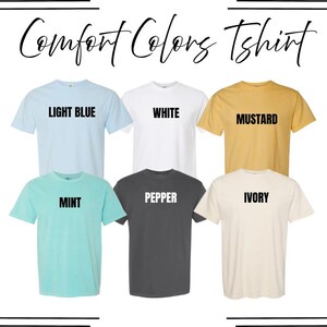 May include: A collection of six short-sleeve crew neck t-shirts labeled Comfort Colors Tshirt. The shirts are displayed in two rows in light blue, white, mustard, mint, pepper, and ivory colors, each with its respective color name printed in black.