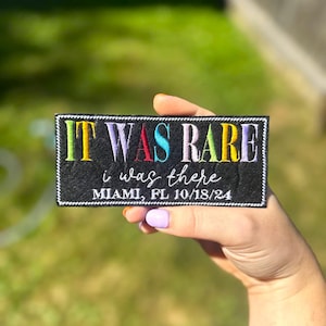 May include: Black embroidered patch with the text "IT WAS RARE i was there MIAMI, FL 10/18/24" in rainbow colors.