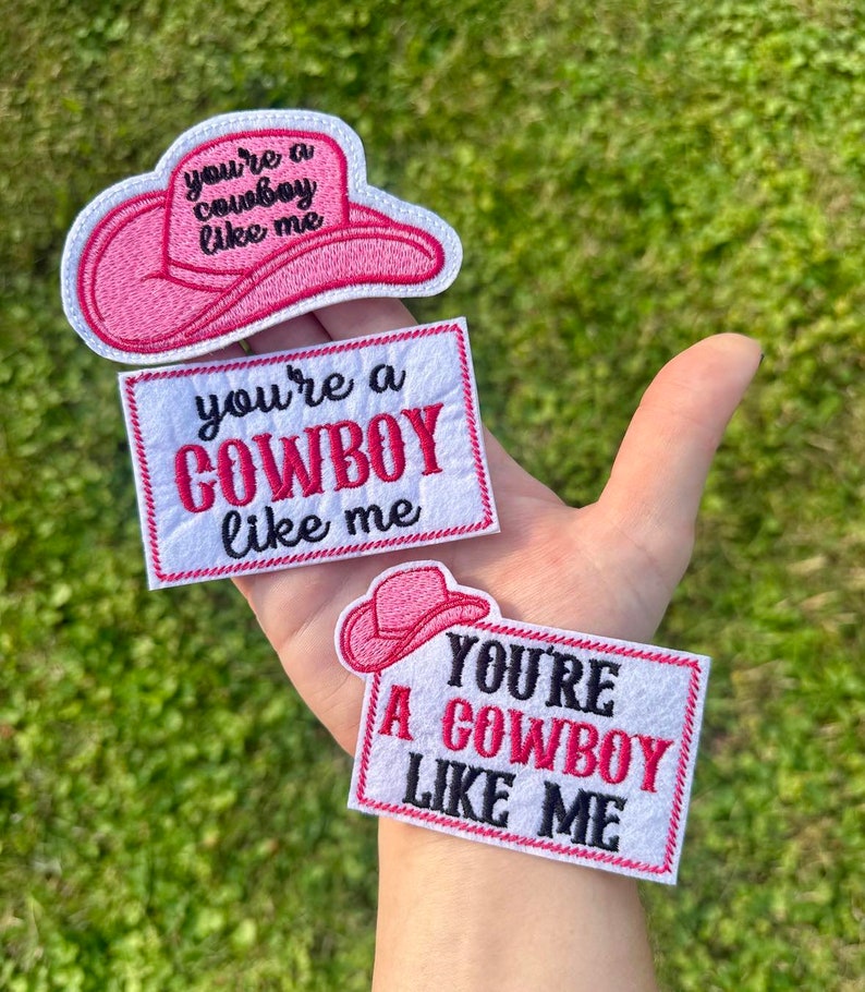 Puede incluir: Tres parches bordados con el texto "You're a Cowboy Like Me". Un parche tiene forma de sombrero de vaquero rosa. Los otros dos son rectangulares con el texto en rosa y negro. Los parches son blancos con un borde rosa.