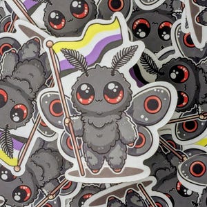 May include: A sticker featuring a cartoon moth holding a non-binary pride flag. The moth is gray with large red-rimmed eyes and a fluffy body. The flag is yellow, white, purple, and black. The stickers are scattered.