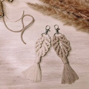 以下が含まれることがあります： 葉のデザインの2つのマクラメキーホルダー。1つのキーホルダーは白、もう1つは茶色です。