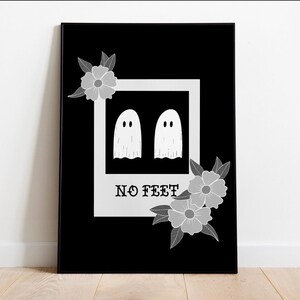Puede incluir: Impresión artística enmarcada en negro con una imagen blanca estilo polaroid de dos figuras de fantasmas y el texto "NO FEET". Acentos florales grises rodean la imagen. La obra de arte se exhibe sobre un suelo de madera.