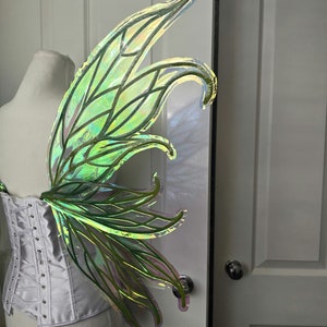 May include: A pair of iridescent green fairy wings with a delicate, intricate design. The wings are made of a translucent material and have a shimmery finish.