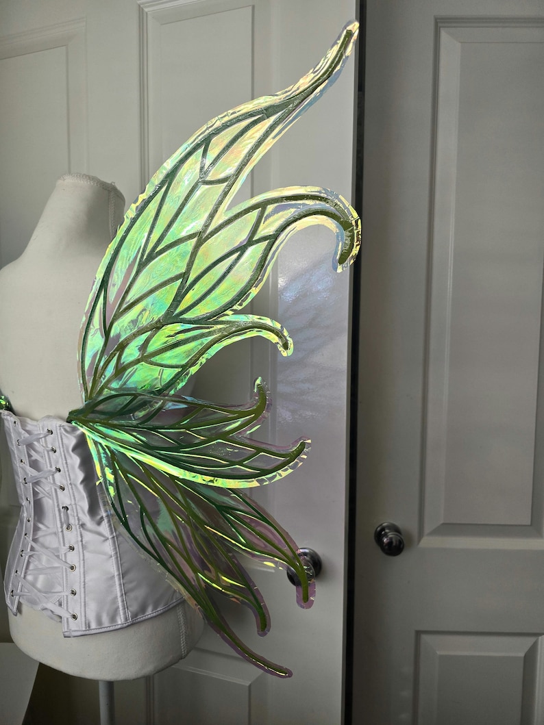 May include: A pair of iridescent green fairy wings with a delicate, intricate design. The wings are made of a translucent material and have a shimmery finish.