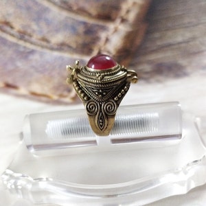 May include: A gold ring with a red stone and intricate details. The ring has a hinged lid that opens to reveal a small compartment.