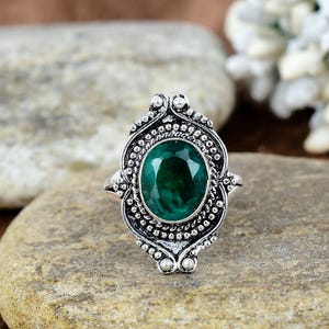 Op de afbeelding: Een zilveren ring met een ovale groene edelsteen gezet in een gedetailleerd, versierd ontwerp.