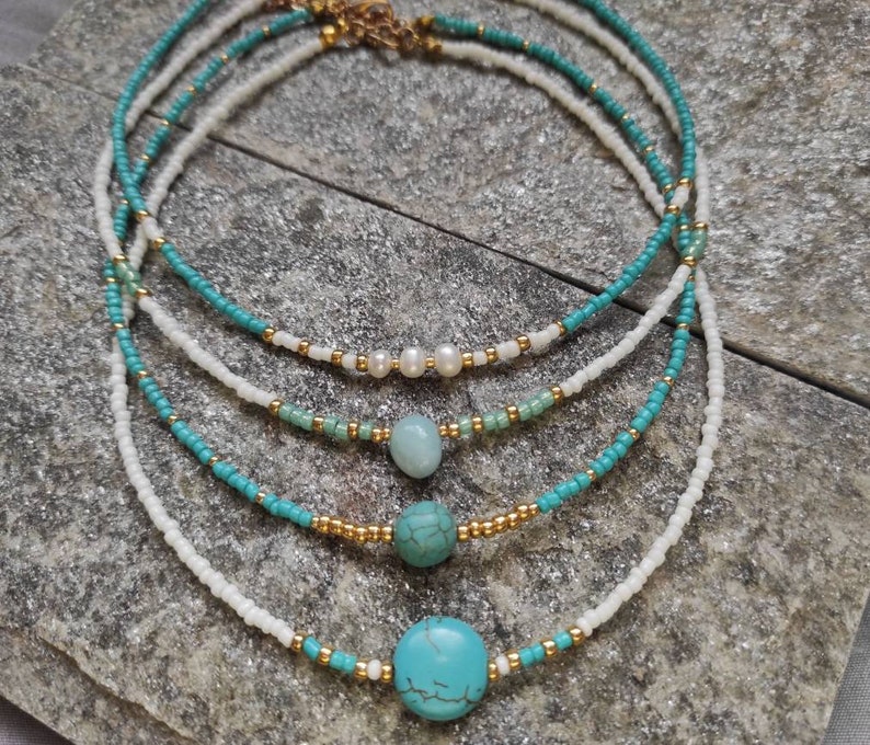 Pu&ograve; includere: Una collana a strati con perline turchesi e bianche. La collana ha una chiusura dorata e presenta pietre turchesi e bianche.