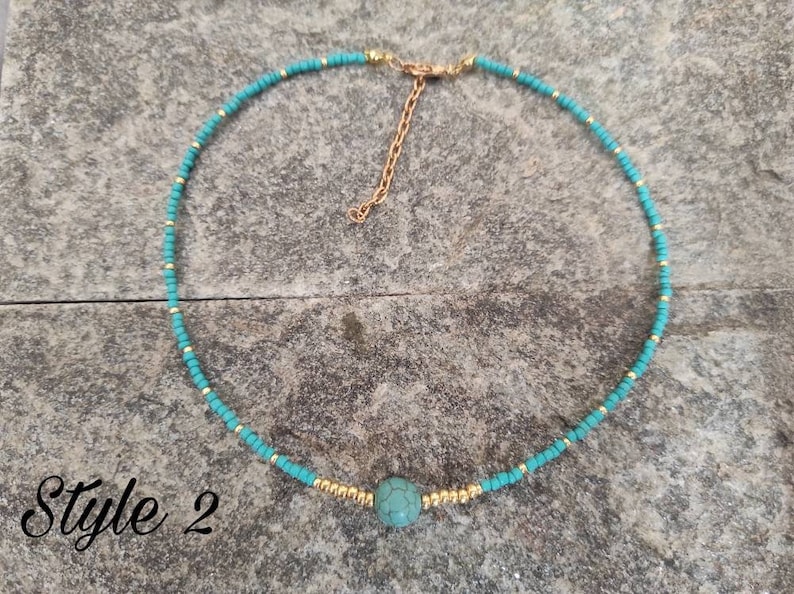 Pu&ograve; includere: Un girocollo con perline turchesi e dorate con un ciondolo in pietra turchese. La collana &egrave; su uno sfondo grigio testurizzato. Style 2.