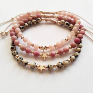 May include: Three layered bracelets with pink and white beads and gold star charms.
