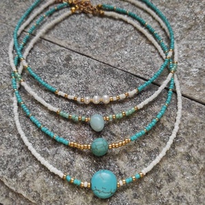 Könnte beinhalten: Eine mehrlagige Halskette mit türkisfarbenen und weißen Perlen. Die Halskette hat einen goldenen Verschluss und verfügt über türkisfarbene und weiße Steine.