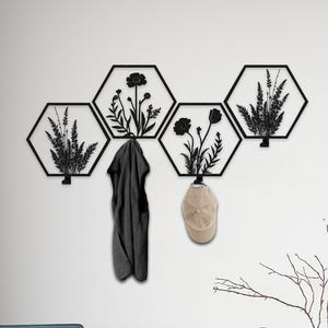 May include: Black metal wall art featuring a series of hexagonal panels with floral designs. A dark gray coat and a tan baseball cap hang from the panels. A blue armchair with wooden legs sits on a cream rug.