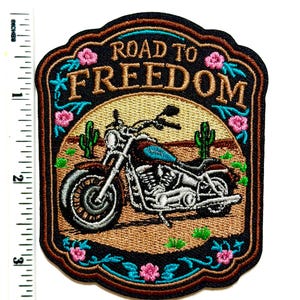 May include: Embroidered patch featuring a motorcycle with the text "ROAD TO FREEDOM". The patch has a brown, black, and turquoise color scheme with desert scenery and floral accents. The patch measures approximately 3 inches in height.