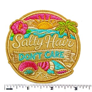 May include: A circular embroidered patch featuring a beach scene with a yellow sun, blue ocean, green palm tree, and pink hibiscus flower. The text reads Salty Hair DON'T CARE. Below are two seashells and a starfish. A ruler shows it is 3 inches wide.