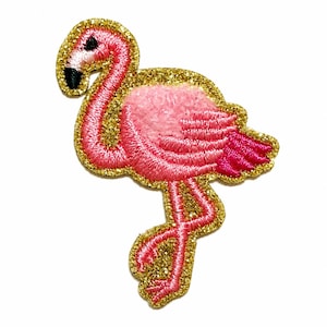May include: A flamingo-shaped embroidered patch featuring vibrant pink thread for the body and neck, a black beak, and a distinct gold glitter border that outlines the entire shape of the bird in a standing position with one leg raised.