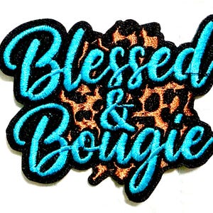 May include: Embroidered patch with the words "Blessed & Bougie" in turquoise script. The text is outlined in black and set against a leopard print background. The patch has a black border.