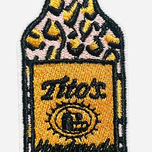 May include: Embroidered patch in the shape of a vodka bottle. The bottle has a leopard print design and a gold label with the text "Tito's Handmade Vodka". The patch is outlined in black.