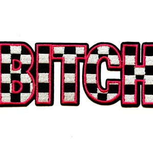 May include: Embroidered patch with the word "BITCH" in bold, block letters. The letters are black with a white and black checkered pattern, outlined in bright pink. The patch is approximately 3 inches wide.