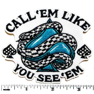 May include: Embroidered patch with the text "CALL 'EM LIKE YOU SEE 'EM". The patch features a blue ace of spades design with a black and white checkered snake wrapped around it. Two spade symbols are on either side.