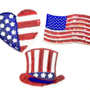 May include: Three decorative patches featuring red, white, and blue sequins. One patch is heart-shaped with stars and stripes, one is a rectangular American flag, and one is a top hat with a star-patterned blue band and red and white stripes.