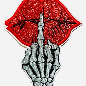 May include: Embroidered patch featuring a red glitter lip design with a skeleton hand giving the middle finger. The patch has a white border and is approximately 2 inches wide.