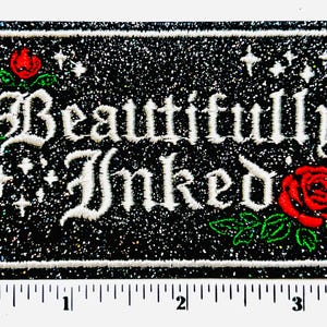 May include: Rectangular patch with the words "Beautifully Inked" in white script. The patch has a black glitter background, white border, and features red roses with green leaves. The patch measures approximately 3 inches wide.
