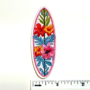 May include: Embroidered surfboard patch featuring a floral design. The patch has a white background with a pink border. The surfboard shape is filled with red, orange, pink, and blue embroidered flowers and leaves. The patch is approximately 2 inches long.