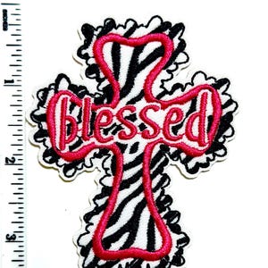 May include: Embroidered cross-shaped patch with a zebra print background and the word "Blessed" in pink. The cross is outlined in pink and has a black and white zebra pattern. The patch is approximately 3 inches tall.