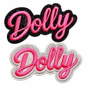 May include: Two embroidered patches featuring the word Dolly in bright pink cursive script. One patch has a black glitter background, and the other has a silver glitter background. Both patches have a thick, raised border that follows the text shape.