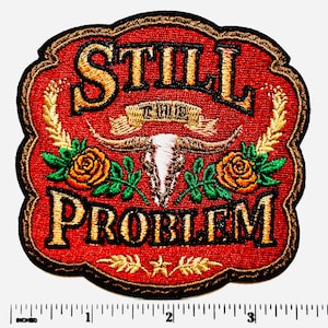 May include: Embroidered patch with the words "STILL PROBLEM" in gold thread on a red background. Features a bull skull, roses, and wheat stalks. The patch is approximately 3 inches wide.