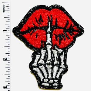 May include: Embroidered patch featuring red lips with a glittery finish and a black outline. Below the lips is a white skeleton hand giving the middle finger. The patch has a black glitter border.