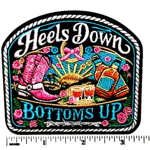 May include: Embroidered patch with the words "Heels Down Bottoms Up" in white and turquoise. The patch features a pink cowboy boot, bottles, shot glasses, and floral accents. The patch measures approximately 3 inches wide.
