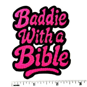 May include: A black embroidered patch with the words "Baddie With a Bible" in bright pink, glittery lettering. The patch is approximately 3 inches wide and 3 inches tall.