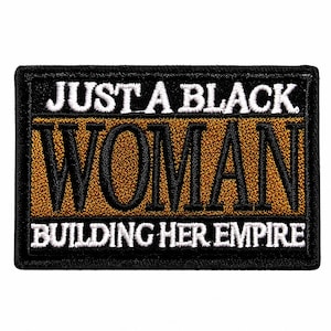 May include: A rectangular embroidered patch with a black border. The text reads JUST A BLACK in white, followed by the word WOMAN in large black letters on a bronze background, and BUILDING HER EMPIRE in white at the bottom.